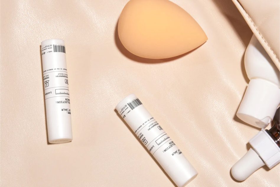 White pump bottle, white tubes, peach sponge on beige textured background