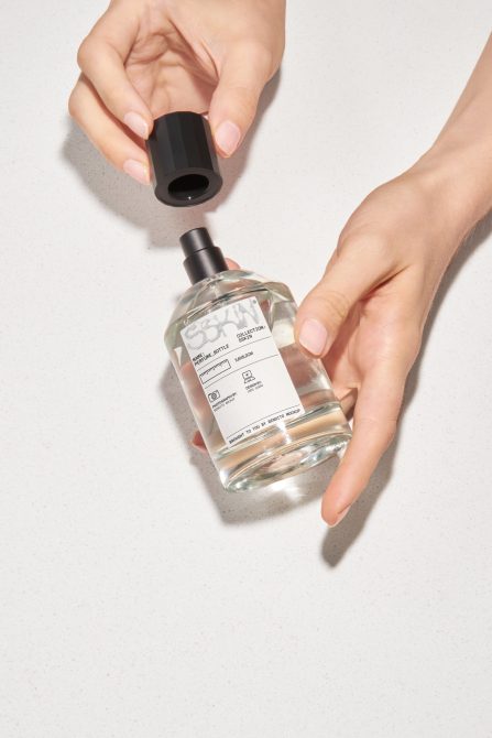 Hands holding a perfume bottle with a removable cap, ideal for mockup template design for branding and packaging presentations.