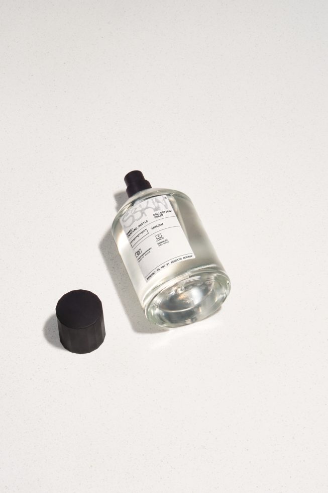 Transparent skincare bottle with label and black cap on a light surface, ideal for beauty product mockups, packaging design.