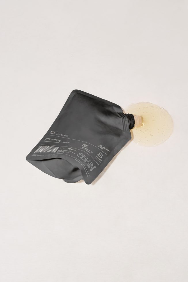 Black squeeze pouch packaging mockup with spilled content, isolated on a light background, perfect for product design presentation.