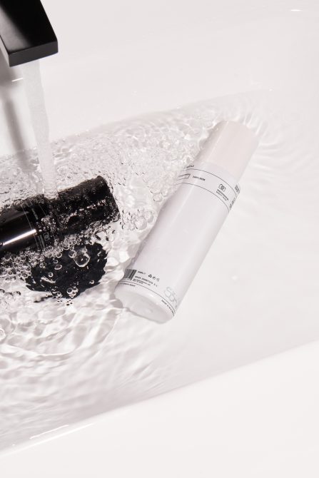 Cosmetic bottles under running water in sink for product mockups, clean minimalist design, ideal for beauty branding presentations.