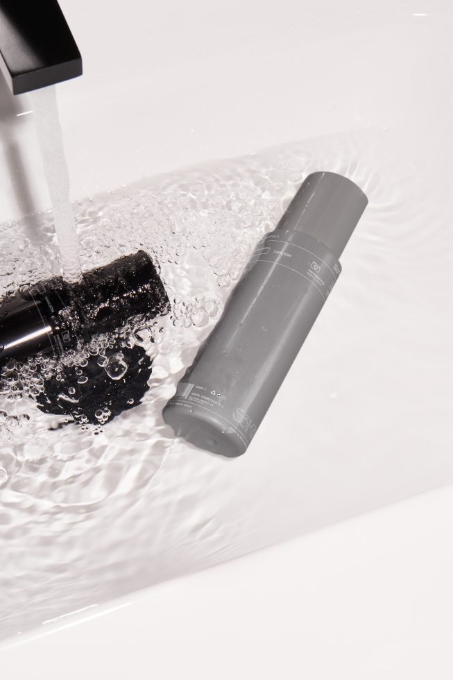 Waterproof product mockup with cosmetic bottle under running water tap, showcasing label durability in sink, ideal for product design presentation.