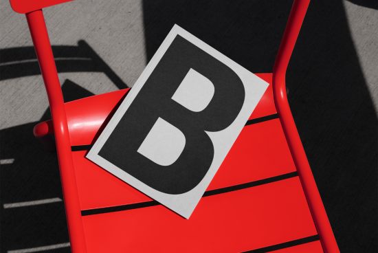 Bold letter B graphic print on paper resting on a vibrant red chair in sunlight casting shadows, perfect for mockup or typography presentation.