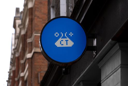 Pixel art style sign mockup attached to building exterior, featuring a retro 8-bit graphic on a blue circle, ideal for urban design templates.