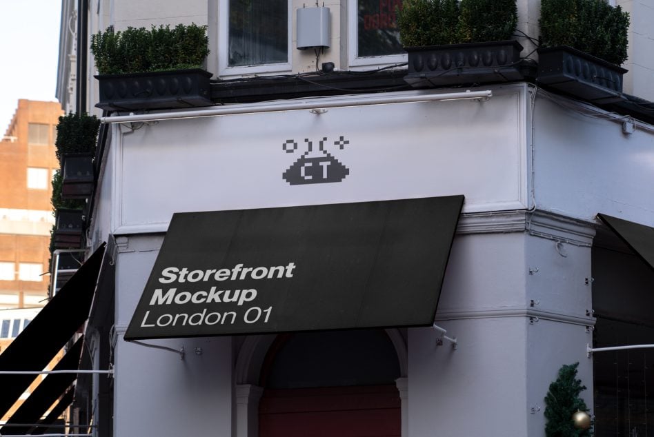 Black storefront awning with pixelated logo, white facade, topiary plants