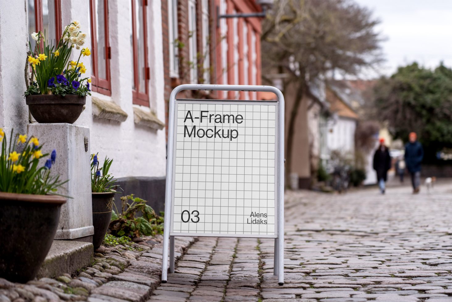 A-Frame sidewalk sign mockup on cobblestone street with people in background, ideal for designers to showcase advertising graphics.