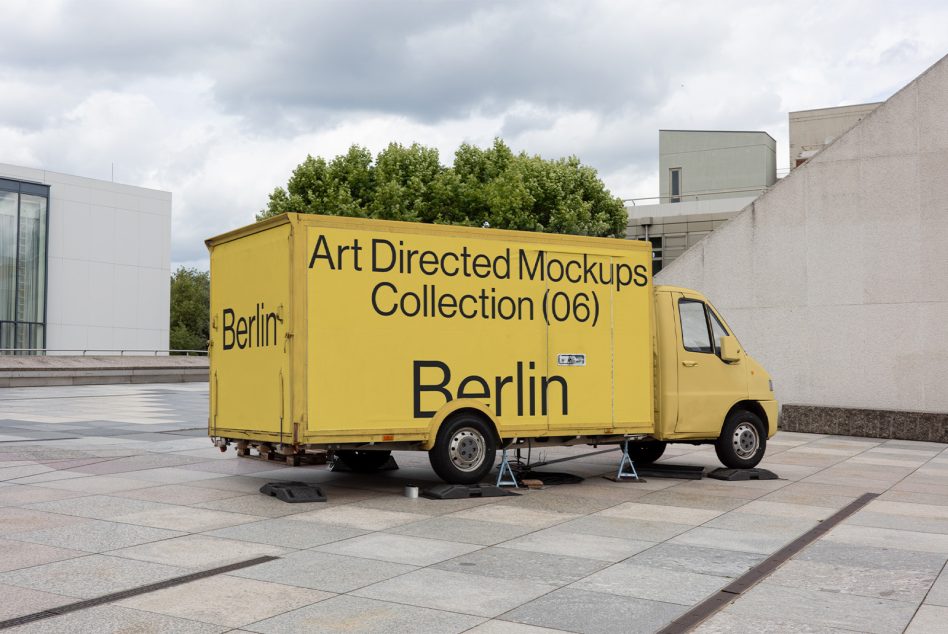 Bright yellow cargo truck in city courtyard with black text on side panel