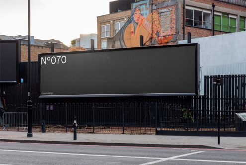 Empty urban billboard mockup for advertising design presentation, with a street art mural in the background, clear sky, and cityscape.