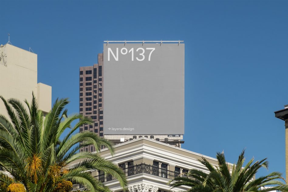 Billboard mockup on urban building used for advertising design presentation, surrounded by palm trees with clear blue sky background.