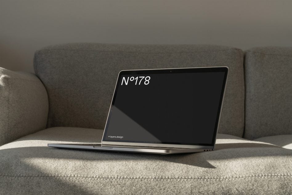 Laptop mockup sitting on a gray linen couch with natural light casting shadows across the screen