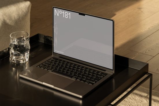 Laptop mockup on a coffee table with a glass of water beside, showcasing screen for design presentation, in a modern interior setting.