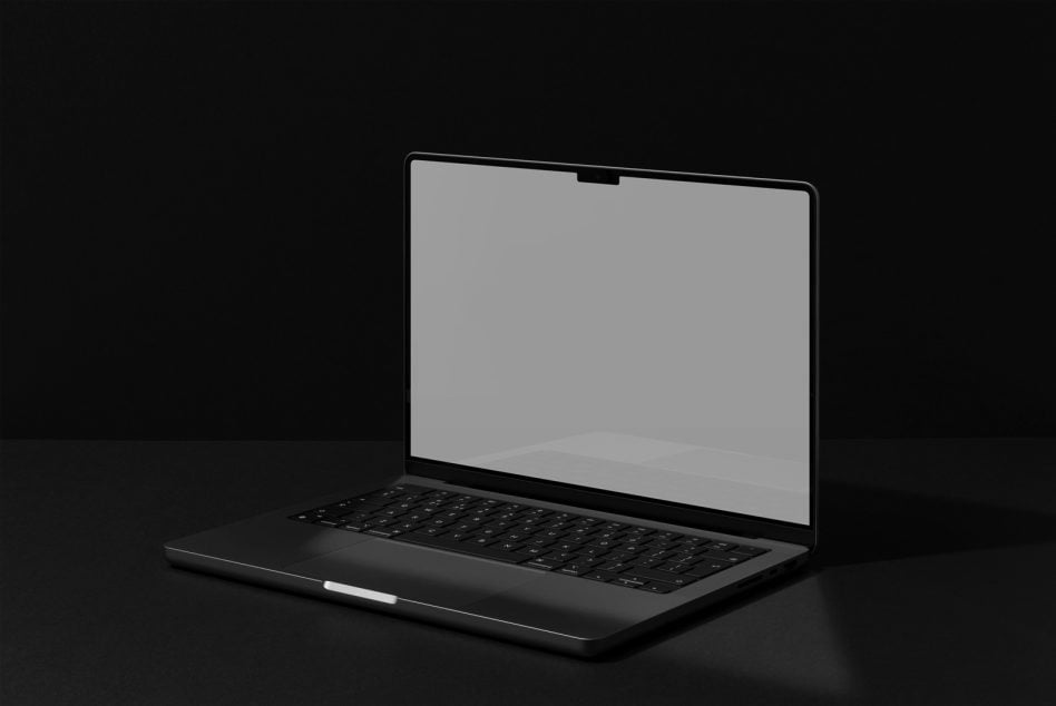 Black laptop with blank screen sitting on dark surface against black background