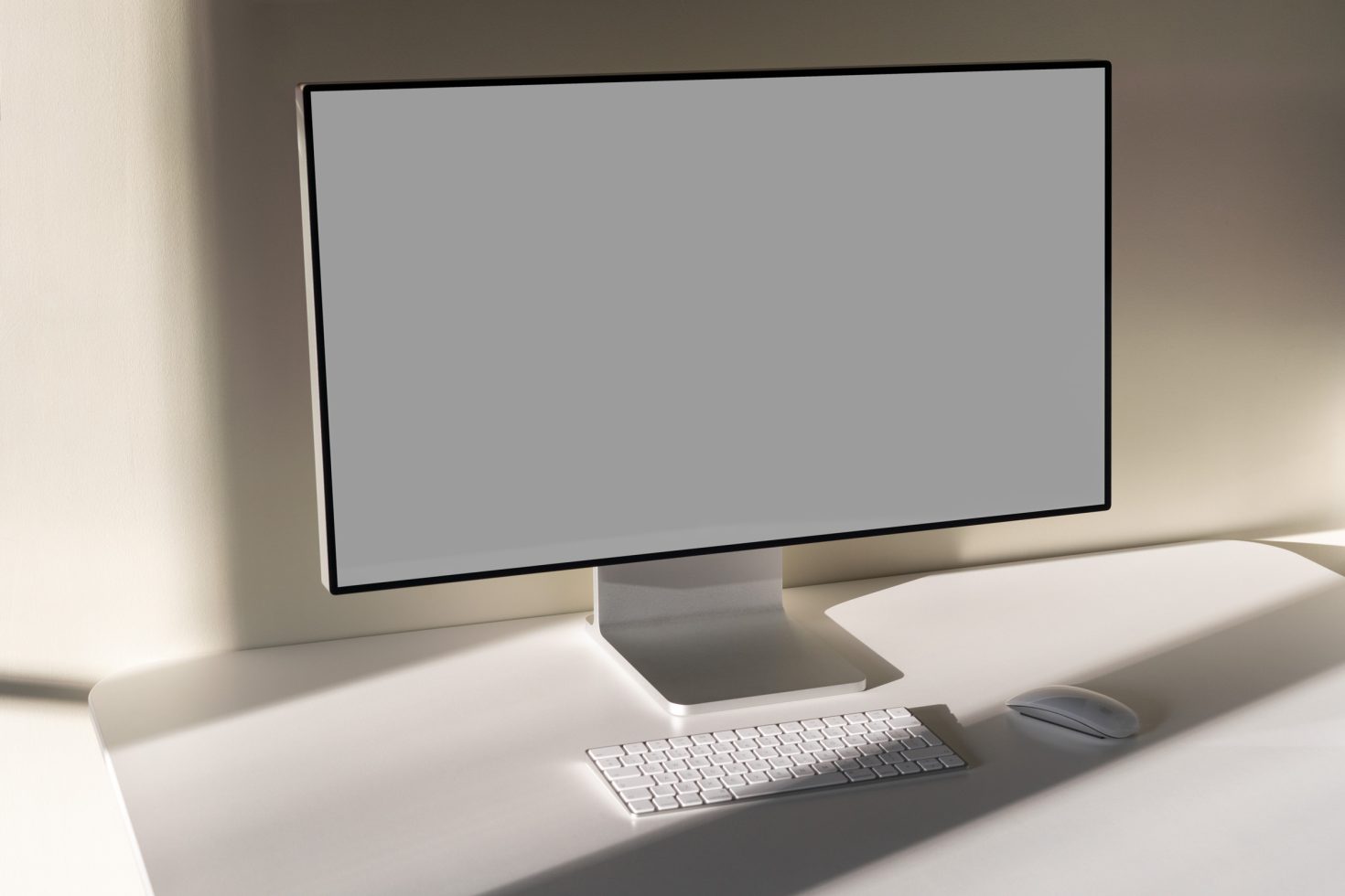 Computer monitor on a desk with keyboard and mouse for mockup display in a sunlit setting, ideal for digital design presentations.