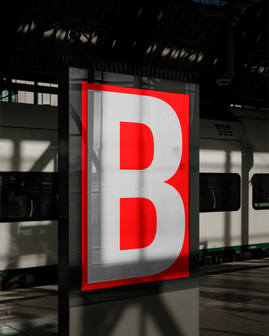 Outdoor billboard mockup at a train station displaying bold red letter B, with realistic shadows and lighting, suitable for advertising and design presentations.