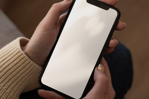 Hand holding smartphone with blank screen mockup for app design display, in a natural indoor setting, ideal for designers digital portfolio.