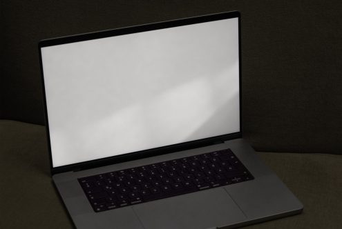 Laptop with blank screen on a dark sofa, ideal for mockup presentations, digital design, web template display, technology and minimalist setup.