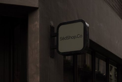 Square shop signboard mockup on building exterior with customizable design space, reflective glass window in dark urban setting for graphic designers.