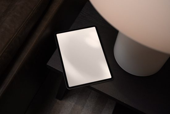 Modern digital tablet mockup on a dark wood table next to a white lamp, with screen ready for design presentation.
