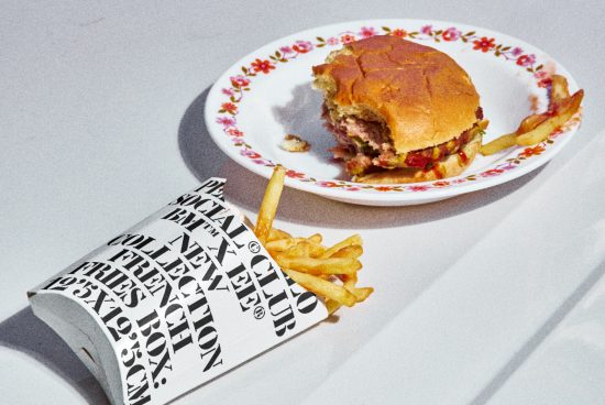 ALT: Half-eaten burger on floral plate, fries spilling from typography printed cup, food mockup, realistic texture, graphic design elements.