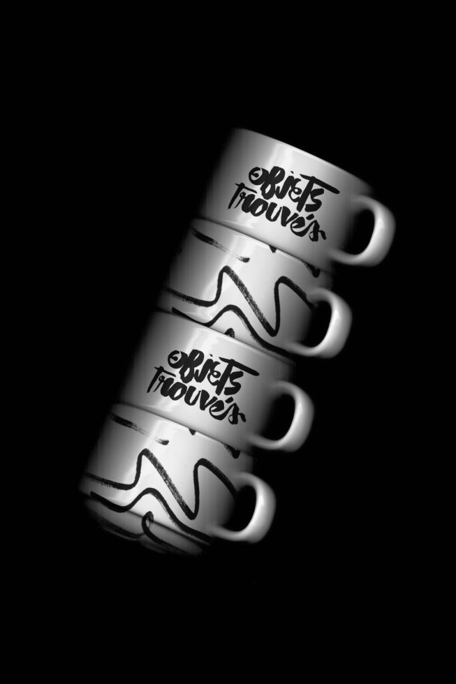 Stacked coffee mugs with stylish typography reflected on a glossy surface in monochrome for mockup or graphic design resources.