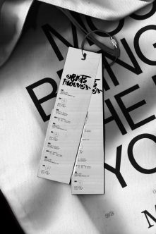 Narrow hang tag on white fabric with black geometric typography overhead shot