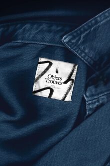 Clothing tag with Objets Trouvés branding centered on deep blue fabric texture