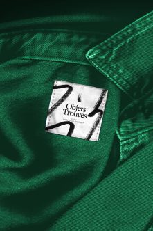 Clothing tag with Objets Trouvés branding centered on emerald green fabric texture