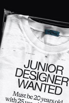 White crewneck tee with 'Junior Designer Wanted' text, blue woven label visible