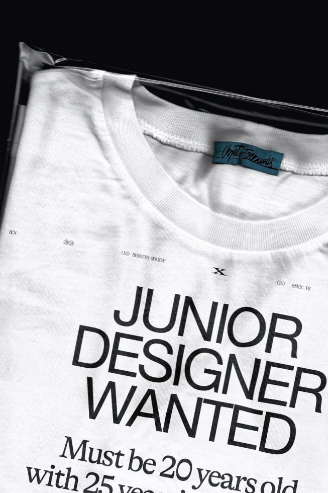 White t-shirt mockup on hanger featuring bold typography design 'JUNIOR DESIGNER WANTED,' ideal for graphics display in designer job ads.