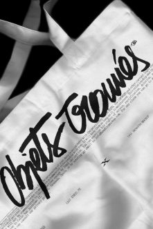 White cotton tote bag with black handwritten script logo in close-up