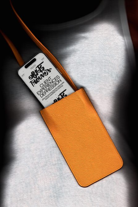 Phone in orange leather case with white label showing brand messaging on sunlit fabric