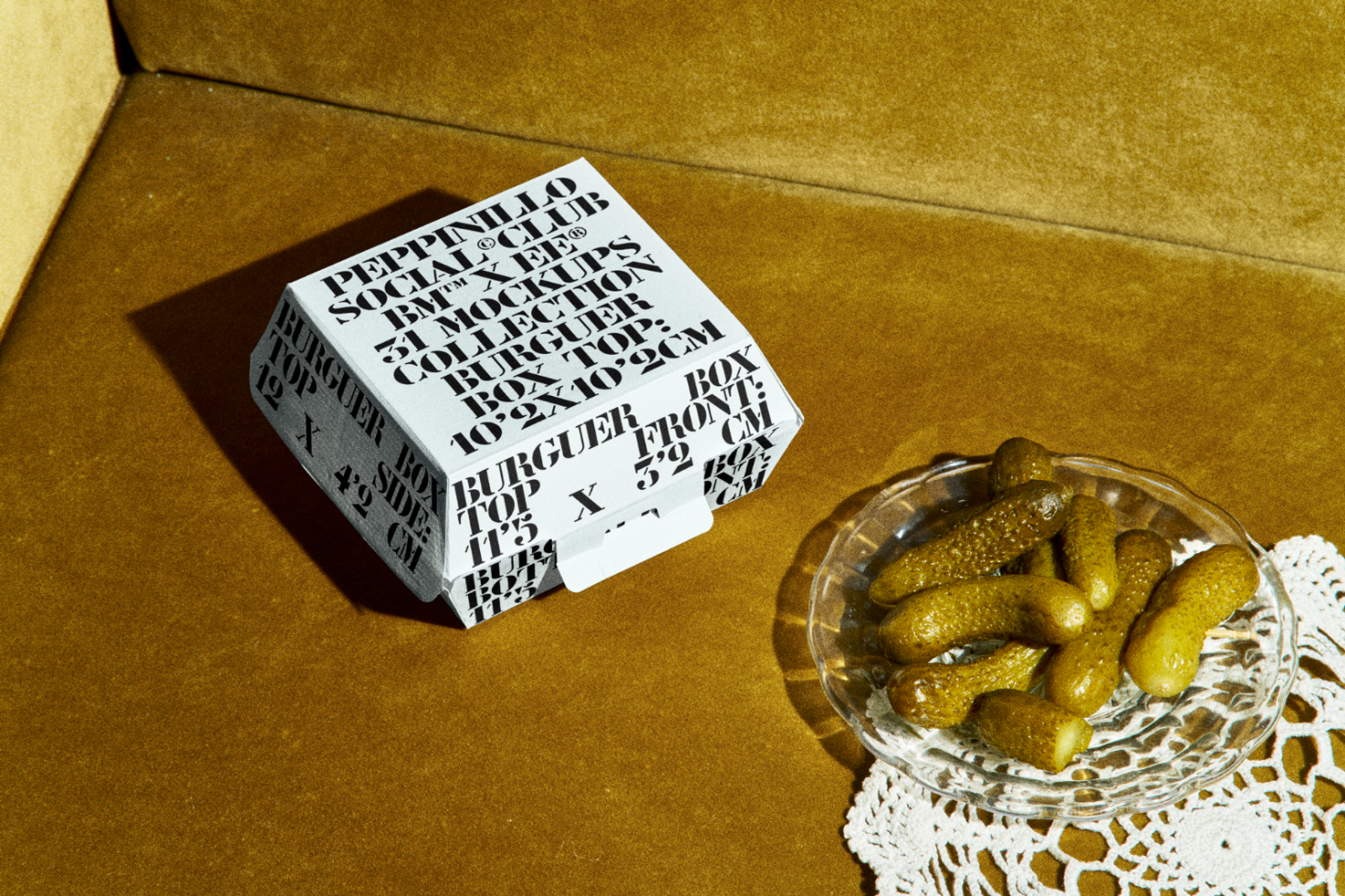 Stylishly designed packaging mockup featuring bold font on a takeout box beside a glass dish of pickles, perfect for showcasing branding projects.