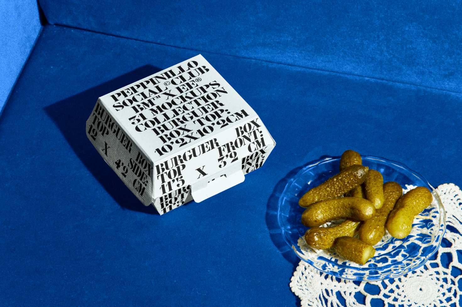 Creative packaging mockup with bold typography design on white box next to gherkins on blue background, ideal for font display and design showcase.