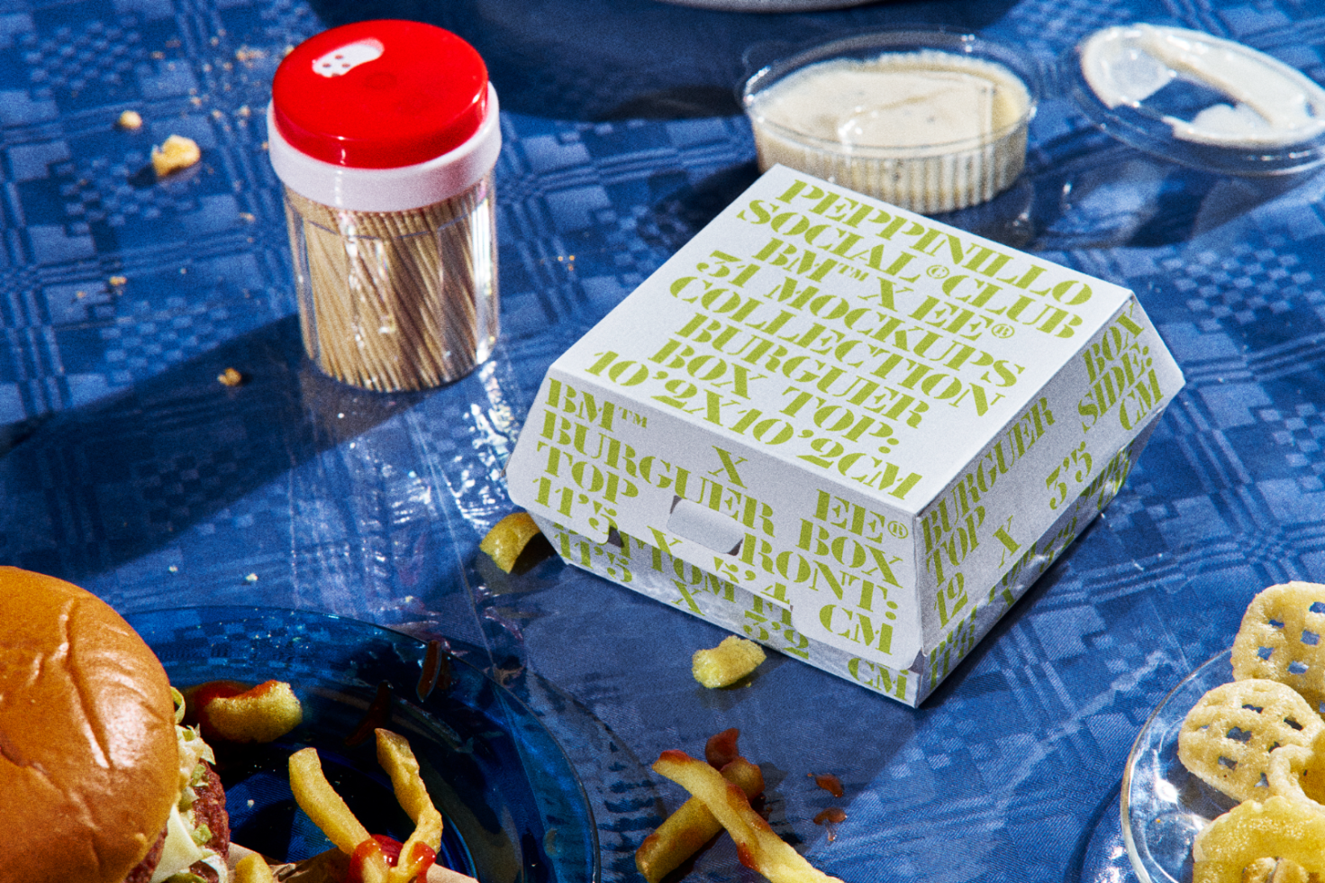 Vibrant burger packaging box mockup with dynamic typography amidst a meal setting, perfect for graphics and templates for food branding.