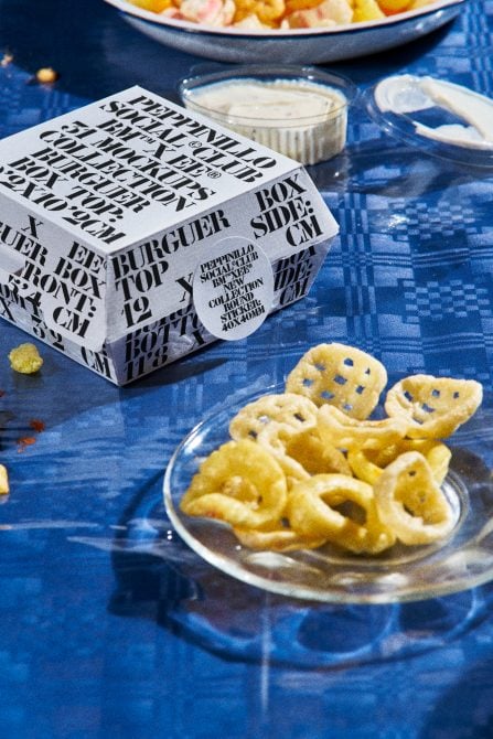 Black typographic food box alongside salted crackers, dip, on blue cloth