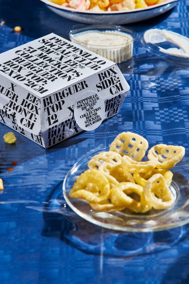 Creative burger box mockup on a blue textured tablecloth with scattered fries and dip sauces, perfect for food packaging design mockups.