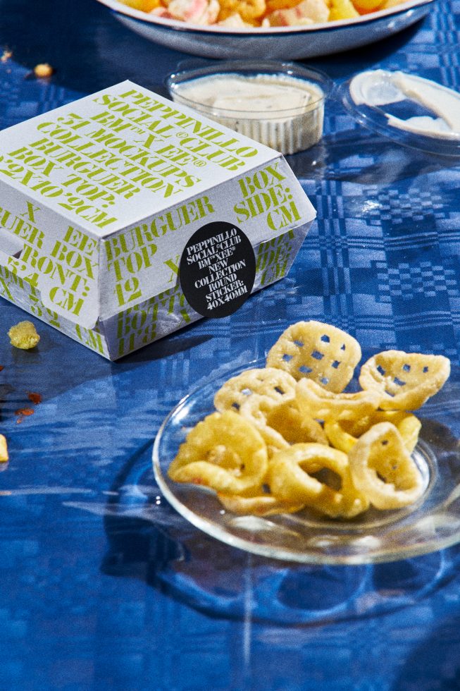 Vibrant fast food packaging mockup with typographic design on a burger box, surrounded by crispy snacks and dipping sauce.