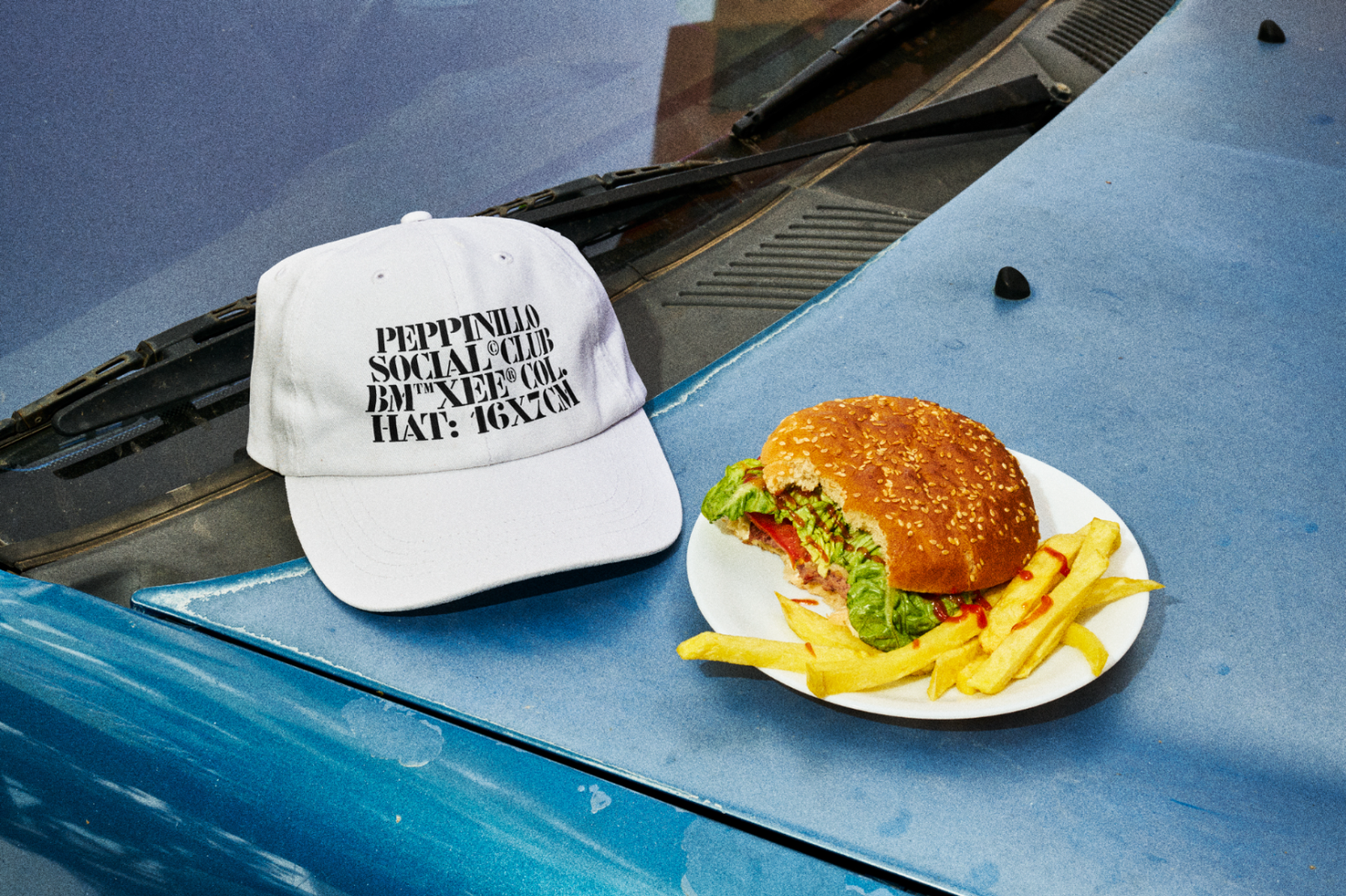 Urban style cap mockup with burger and fries on a car hood, ideal for streetwear branding presentations.