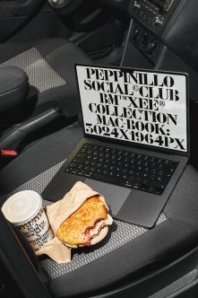 Laptop in car seat displaying bold typography mockup with coffee cup plus sandwich nearby