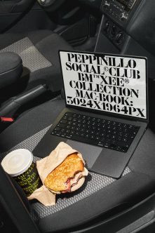 Laptop in car seat showing bold serif typography mockup with coffee cup plus sandwich nearby