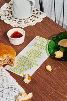 Bent mockup card in lime green text on wood table with burger crumbs, jam cup, cookies