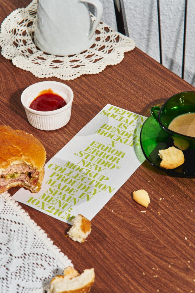 Printed paper with green font design mockup on wooden table with food items, textile, and cup, ideal for designers looking for realistic stationery or menu mockups.