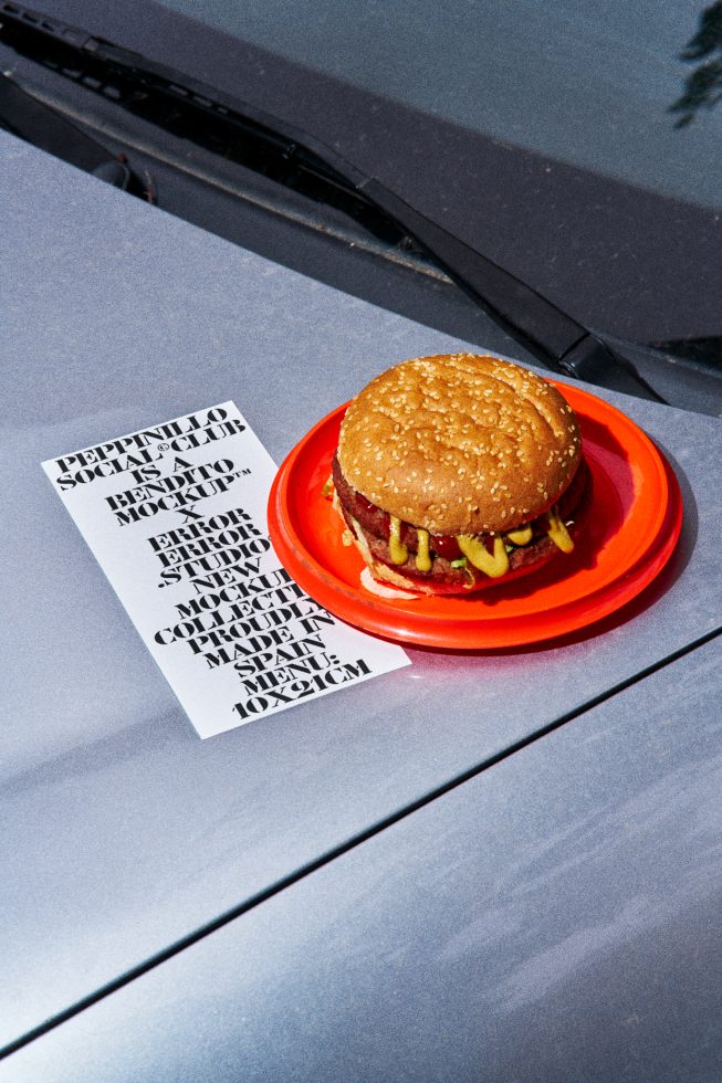 Mockup of a burger on red plate with typographic flyer on car hood for food-related design presentation, showcasing fonts and layout.