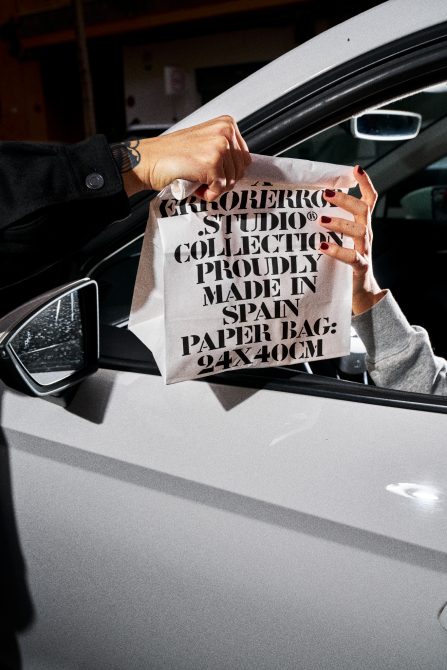 Person holding paper bag with typography design, mockup for graphic designers, packaging branding in urban setting.