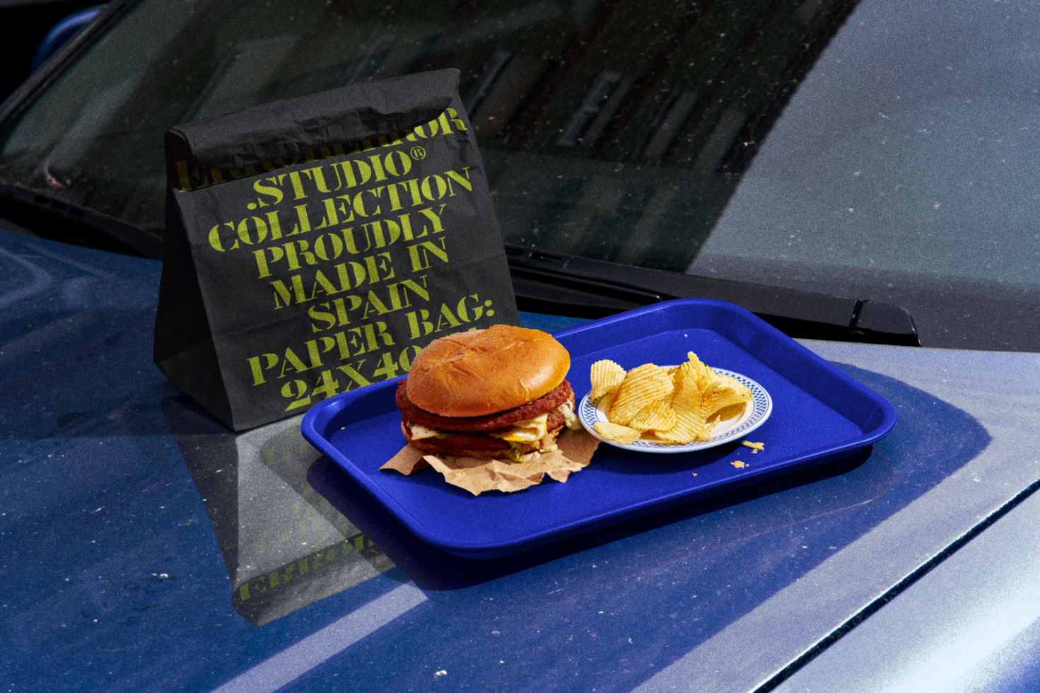 Photorealistic mockup of burger and chips on a blue tray with a branded paper bag, perfect for food packaging design presentations.