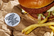 Light blue circular sticker with black text on kraft paper next to burger in paper wrapper