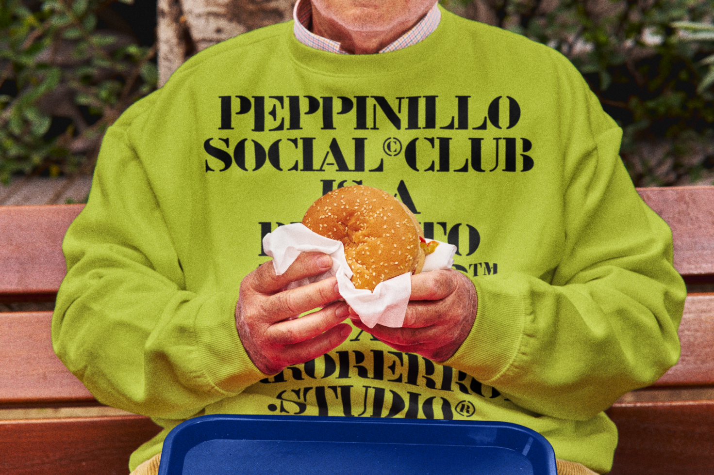 Person in vibrant green sweater with bold text design holding a sandwich, urban setting, ideal for mockup graphics.