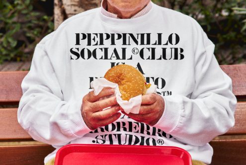 Person in branded sweatshirt holding burger, sitting on bench, detailed texture, realistic mockup for apparel design presentation.