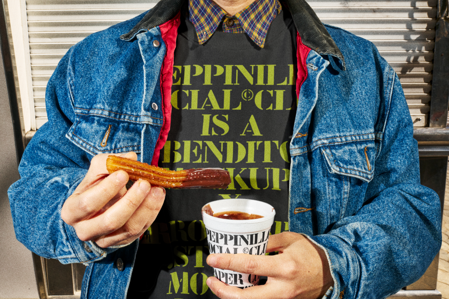 Person in denim jacket holding churro and dipping sauce with graphic design t-shirt mockup. Realistic street style apparel for product display.