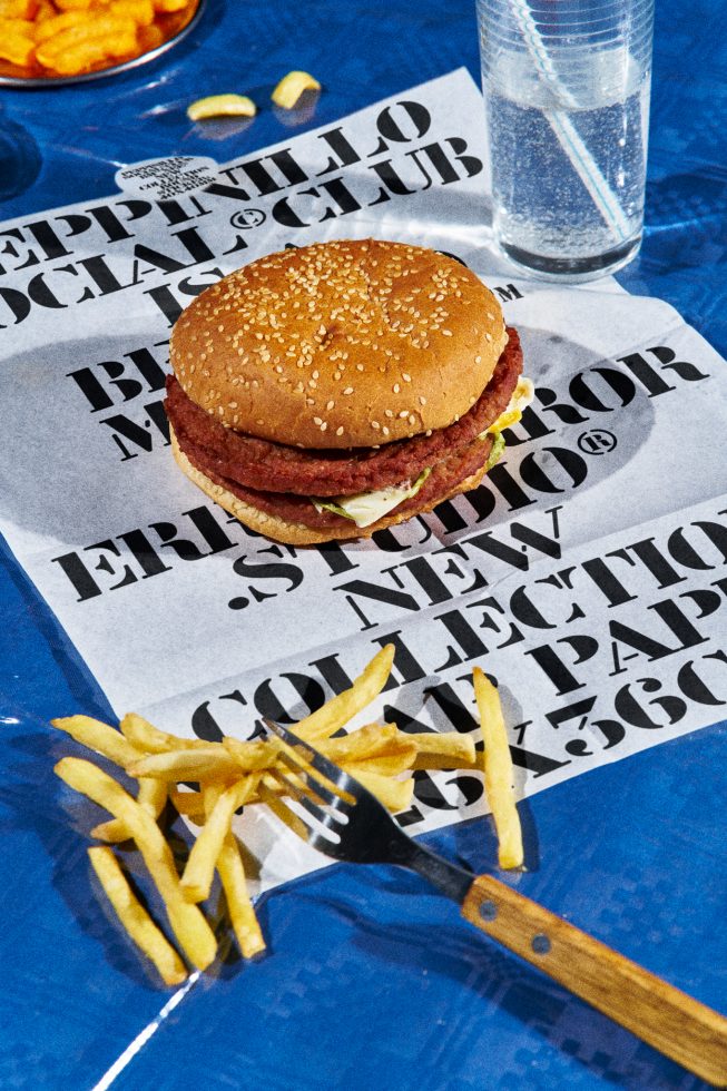 Realistic hamburger and fries mockup on printed paper with water glass, vibrant blue background, food presentation, high-detail photography.